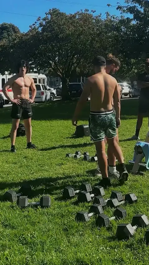 Dom’s small group in a sunny park between sets, dumbbells laid out on the grass