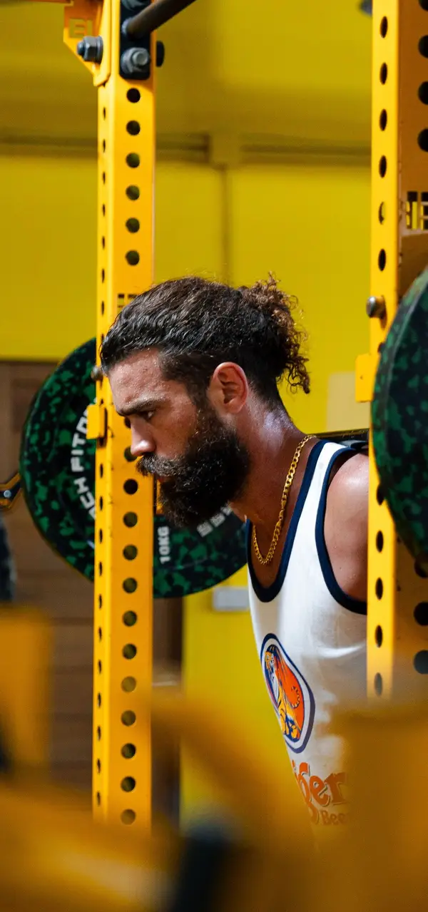Dom set under a loaded squat bar in a yellow rack, in profile